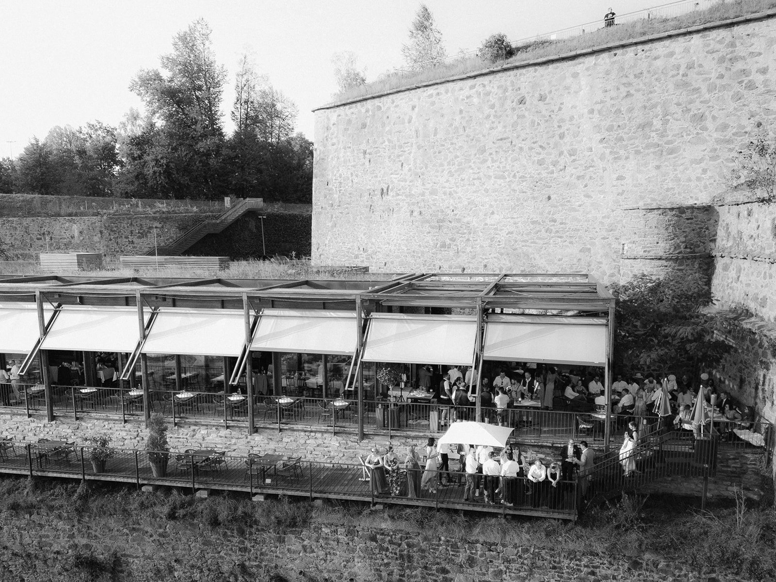 Hochzeitsgesellschaft auf der Terrasse an einer alten Festungsmauer, aus der Luft, Schwarzweiß